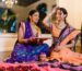 Mother and daughter performing a traditional Indian ritual indoors, wearing colorful sarees.